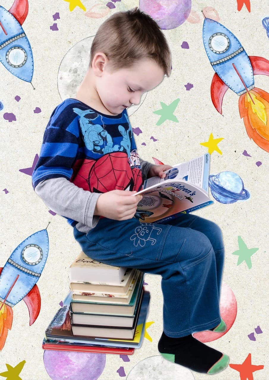 Young boy sitting on books reading a book
